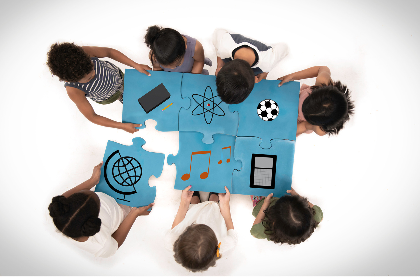 Aerial shot of elementary students fitting curriculum-themed puzzle pieces together.